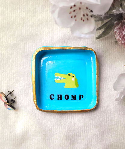Blue trinket dish with an alligator on the in the middle. The text says chomp.