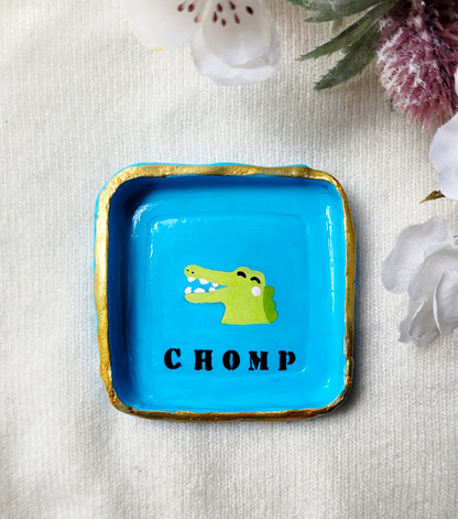 Blue trinket dish with an alligator on the in the middle. The text says chomp.