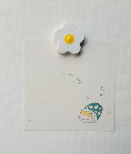 Flower-shaped object with a yellow center on a white card with a cat illustration