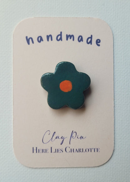Flower-shaped clay pin on a 'handmade' card with 'Here Lies Charlotte' branding.