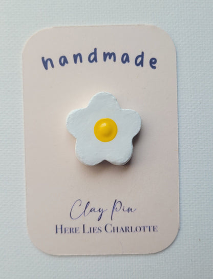 Flower-shaped clay pin on a 'handmade' card with 'Here Lies Charlotte' branding.